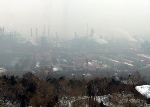 Trees in foreground, buildings and smokestacks beyond.