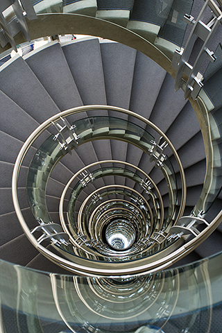  View from the top and down the center of a spiral staircase, made of concrete and glass.