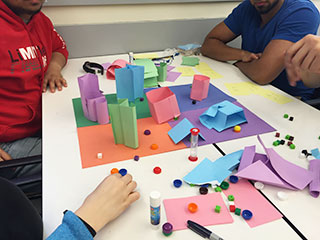 Students sitting around a homemade board game with several game pieces on it.