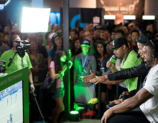 Gamers playing a video game at PAX 2015 while spectators watch.