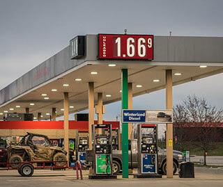 A photo of a gas station with the price of gas displayed. A pickup truck hauling an ATV is in the background. 