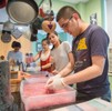 Four glove-wearing students stand over plastic water-filled containers filled with a pink, cotton-like substance.