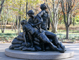 A bronze monument depicting a nurse tending to a wounded soldier, while another nurse looks towards the sky.