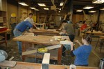 A student in the foreground uses a spokeshave in a tight curve near the bow of her model.