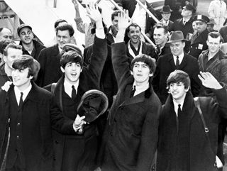 Four men on the tarmac at JFK airport waving to a crowd.