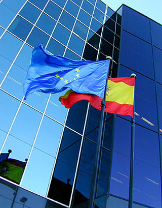 Flags of the European Union and Spain wave outside an office building.