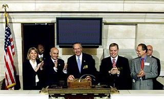 Seven people standing in front of the podium above the trading floor of the New York Stock Exchange.