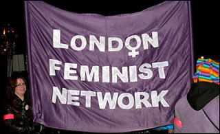 A woman holds a huge purple banner with the words London Feminist Network written on it.