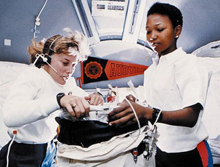 Two female astronauts work on an experiment onboard a space shuttle. 