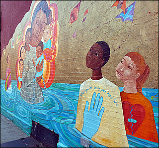 A photographA mural painted on a wall features a body of water in which an African-American boy and a Caucasian girl stand.  The image of a woman surrounded by children is next to them. of a pregnant woman, in a blue shirt, holds her belly.