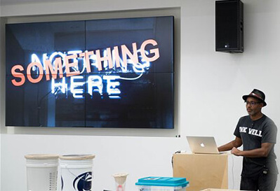 A man stands behind a lecturn next to a screen that says Something Here.