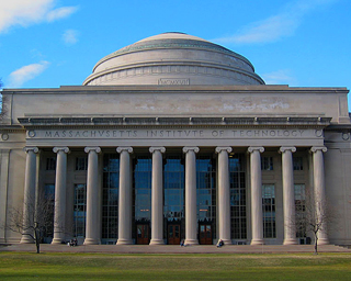 Building with ionic columns and large dome shown from a grassy courtyard.