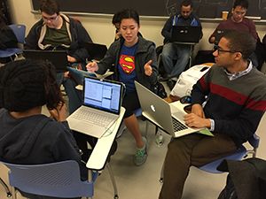 Several students with laptops sitting in close proximity. One of them is gesticulating.